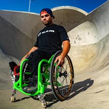 aaron sitting in wheelchair in front of drop ramps at a skate park